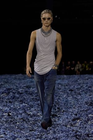 Model in sleeveless grey tank and jeans walks runway covered in blue material.
