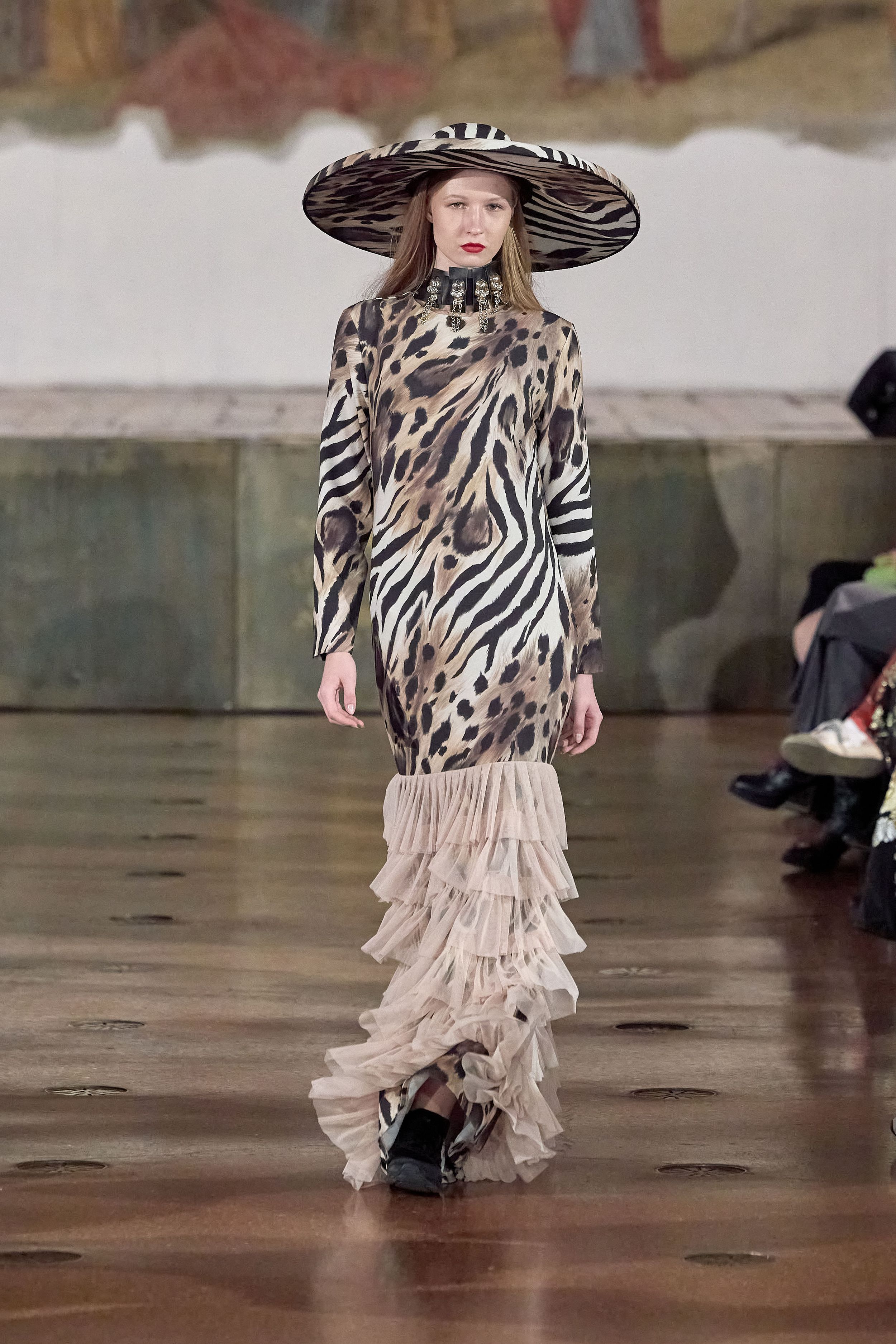 Runway model in zebra print dress with dramatic wide brim hat and ruffled hem.