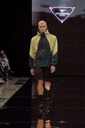 Model presents sporty yellow and black outerwear on dark reflective runway.