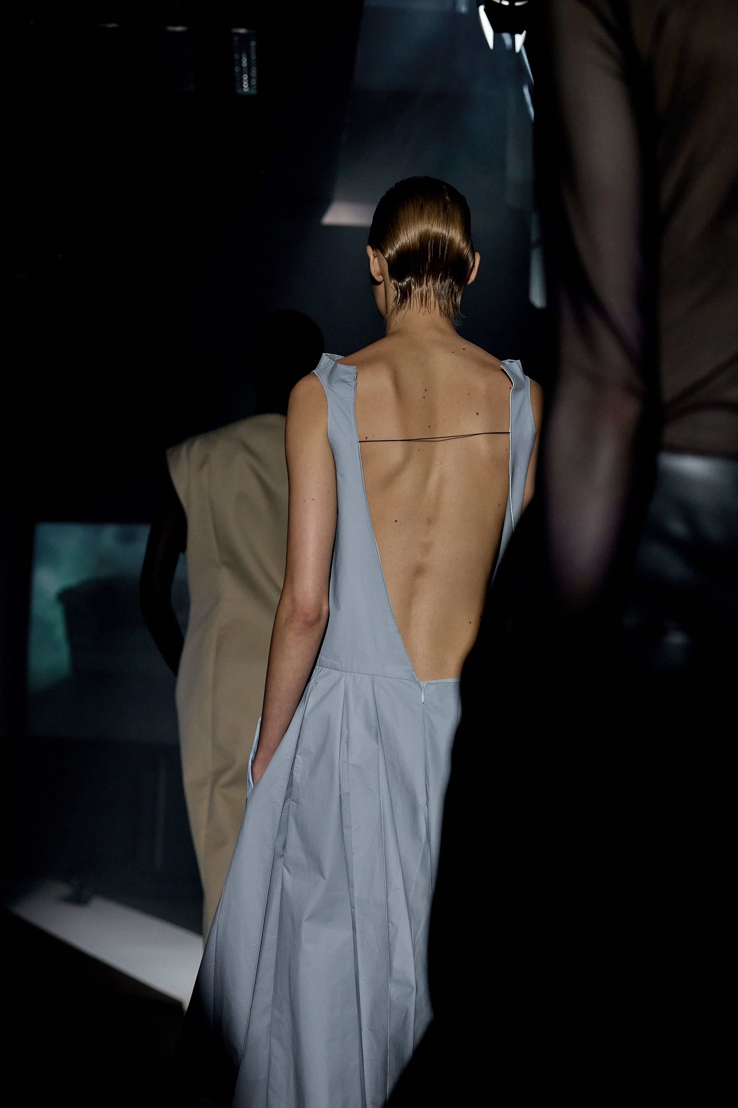 Back view of grey backless dress on runway with sleek updo hairstyle.