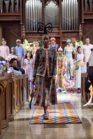 Model walks church runway wearing colorful patterned dress with geometric designs.