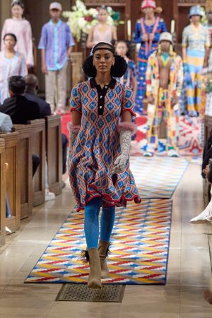 Fashion show featuring geometric print dress with earmuffs and boots on colorful runway.