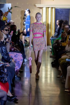 Pink patterned two-piece outfit displayed on illuminated fashion runway.