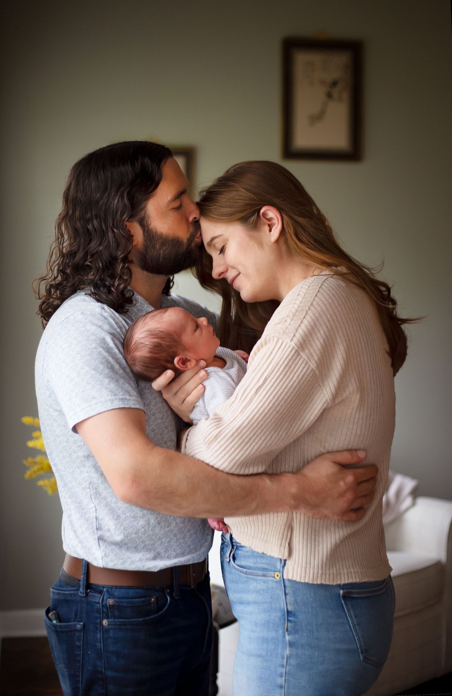 An intimate family moment as parents embrace with their newborn baby in a dimly lit room.