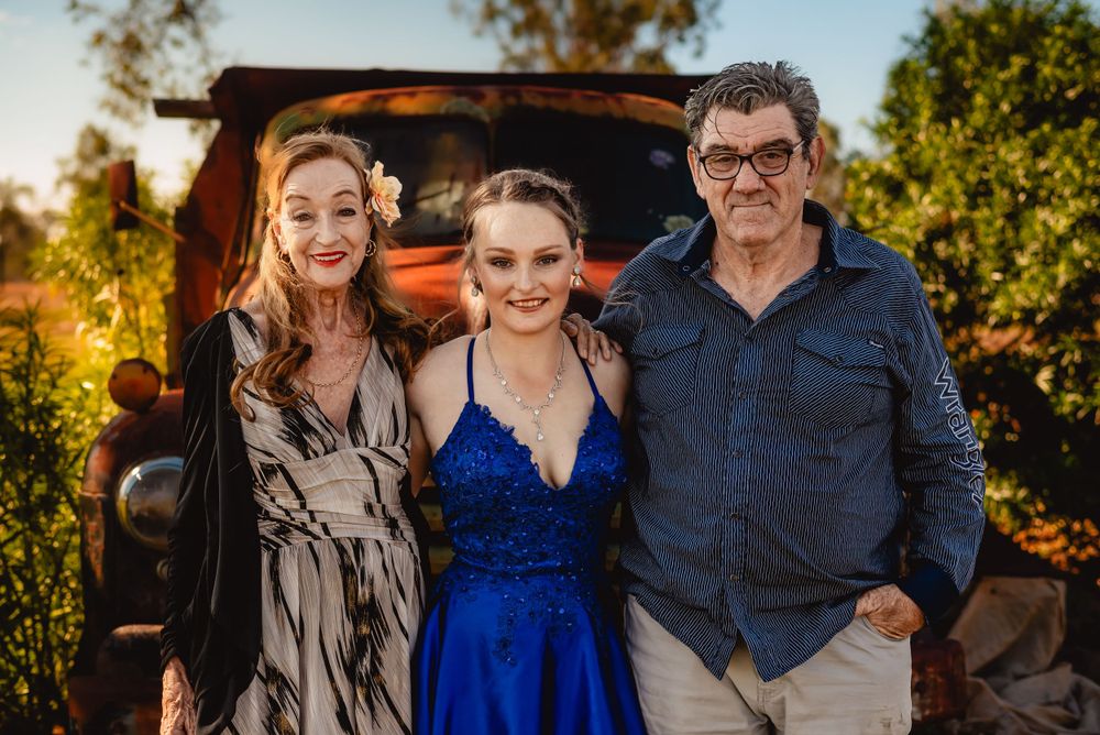 A formal portrait in front of a vintage rusty truck at sunset with a blue gown and casual attire.