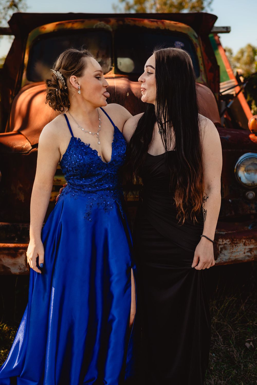 Two people in formal wear share a candid moment in front of a rustic orange truck.