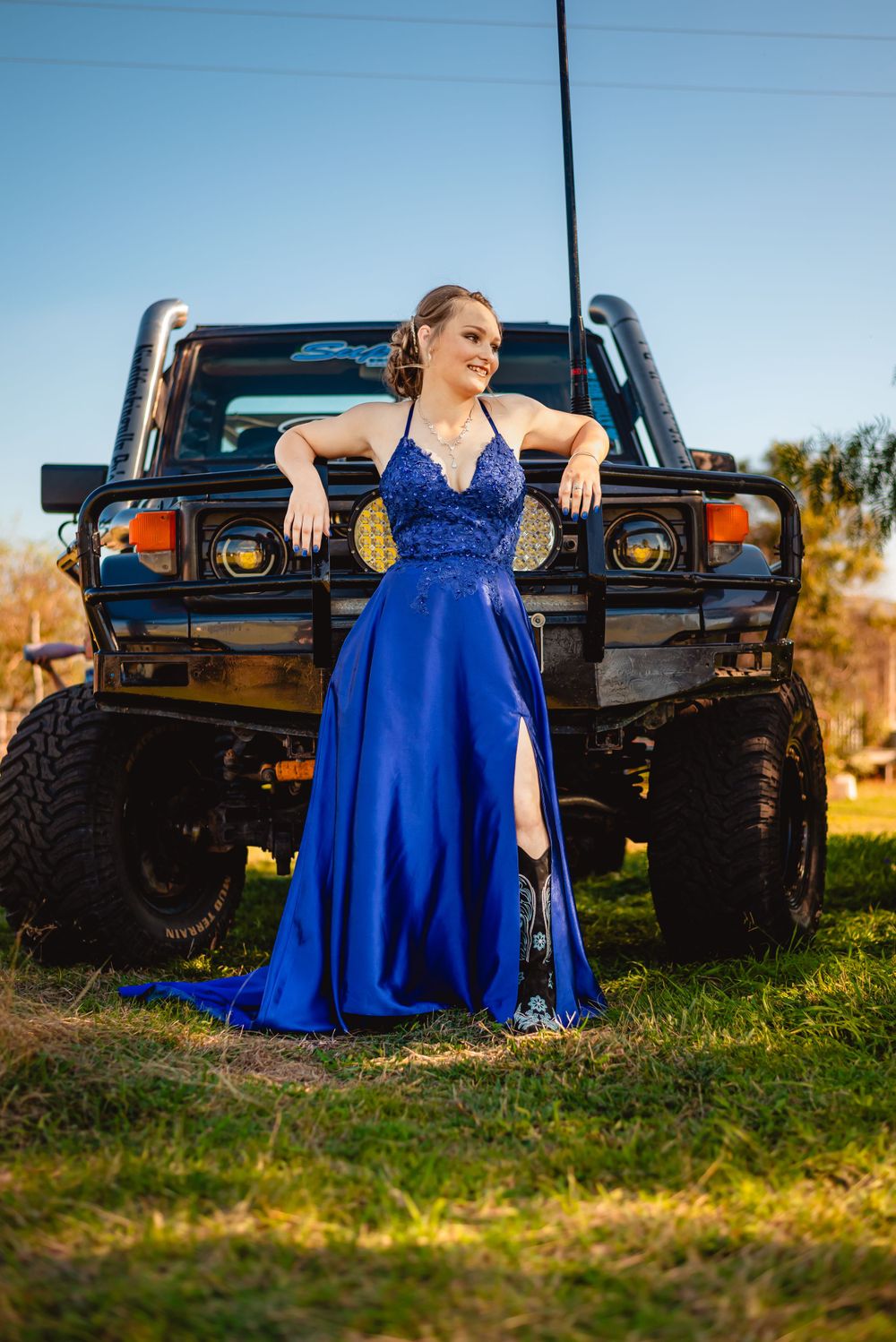 Person in blue formal gown poses in front of lifted black off-road vehicle.