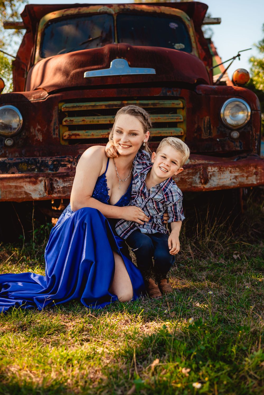 Two people pose together in formal attire by an old rusty truck.
