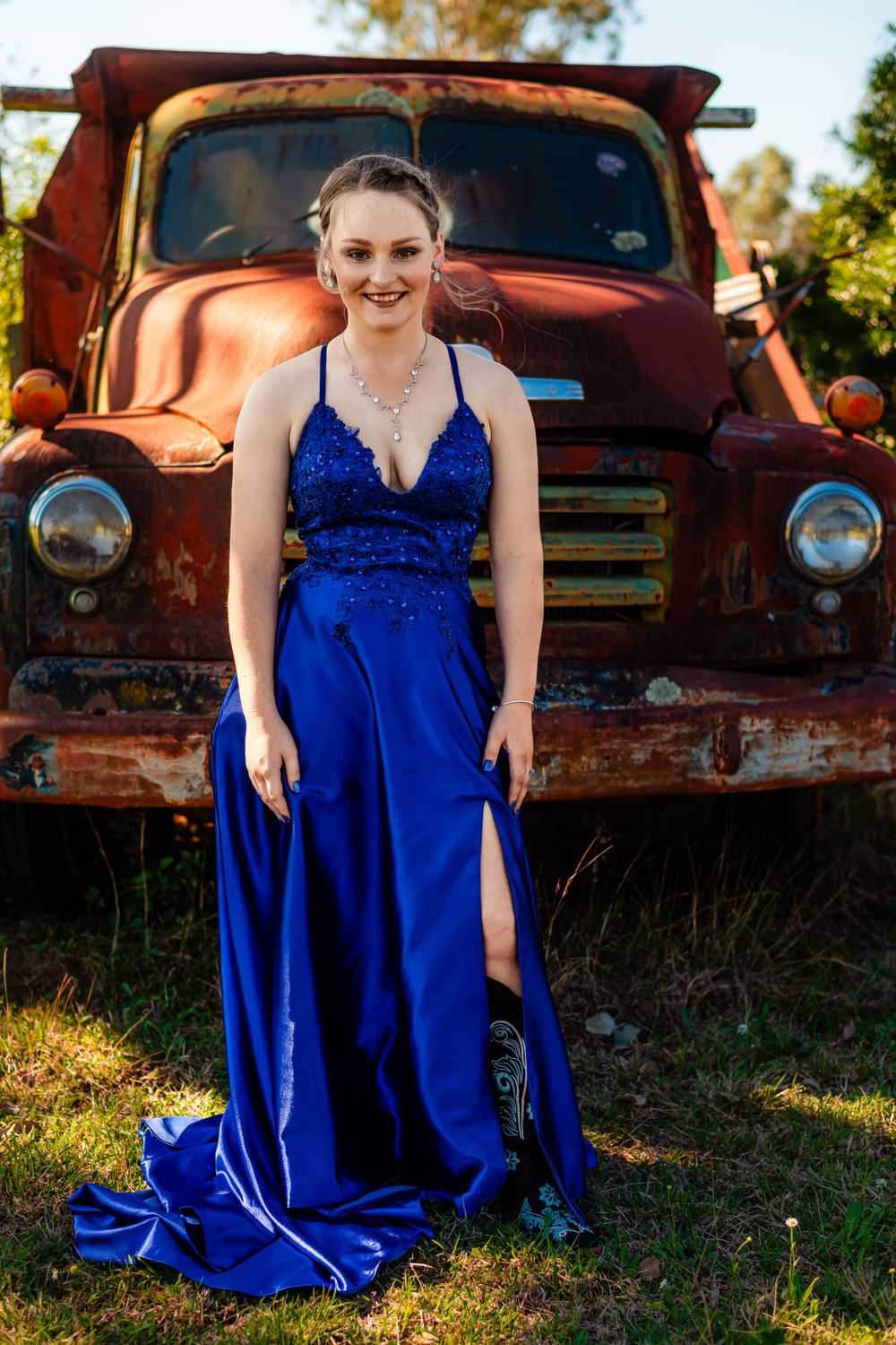 Full-length portrait in a flowing royal blue gown beside a classic rusty truck.