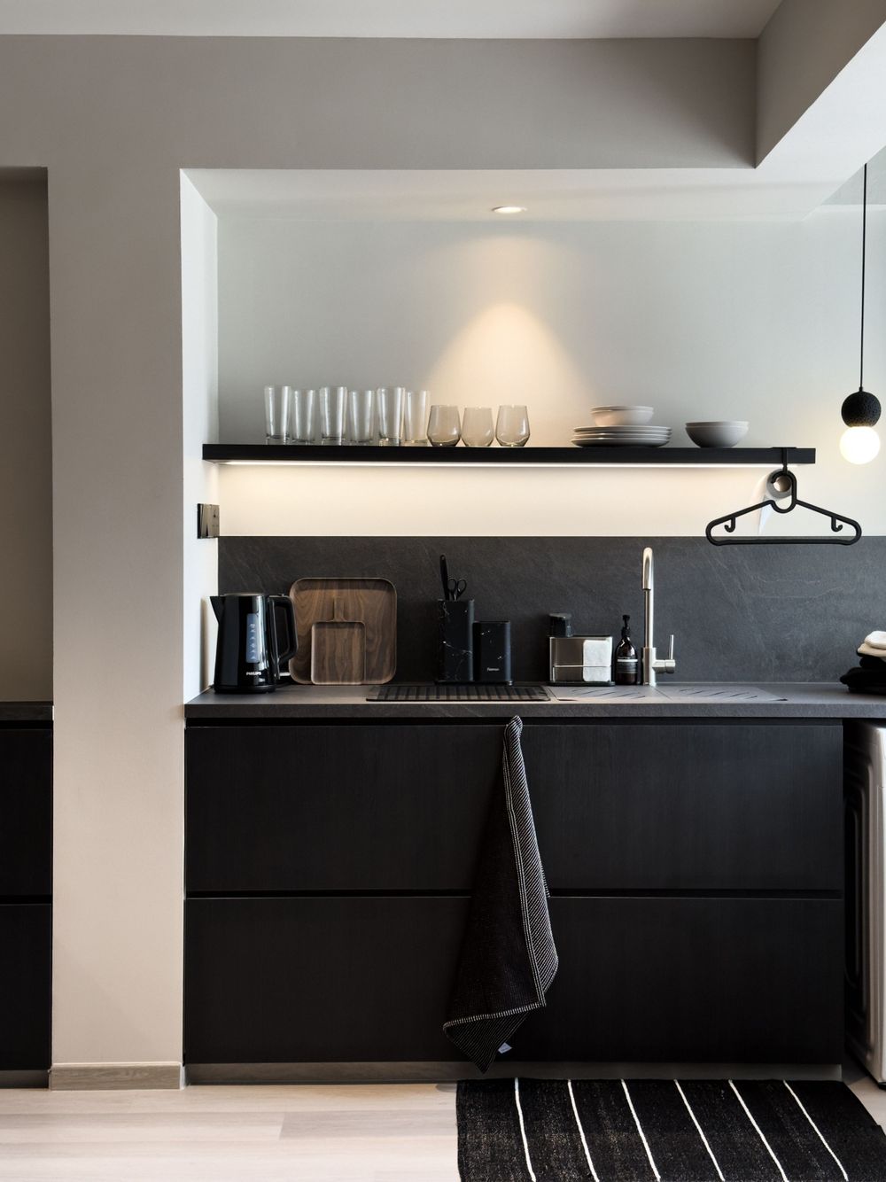 Minimalist kitchen space with black cabinets, floating shelves displaying glassware, and modern appliances.