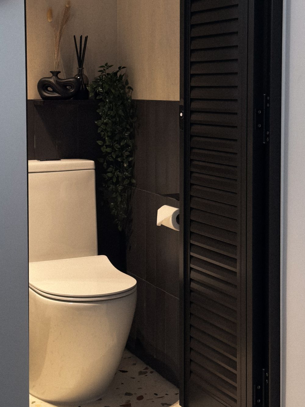 Modern bathroom with white toilet, black wall panels, and decorative green plant in a sleek minimalist design.