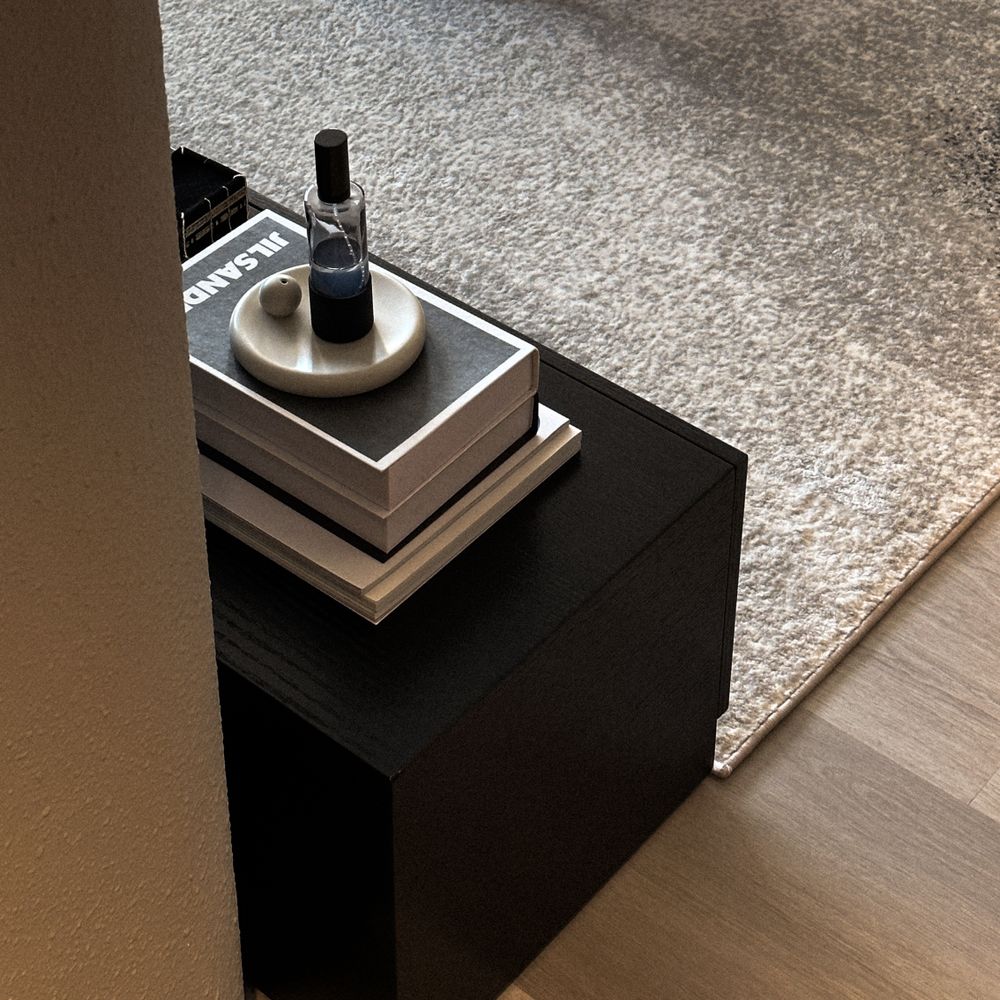 Minimalist side table with stacked books and decorative black accessories on grey carpet.