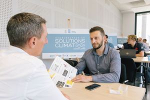 Two people meeting at a table with San Francisco Climate signage visible in the background.