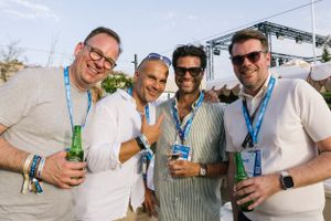 Group of friends holding drinks at an outdoor festival wearing lanyards.