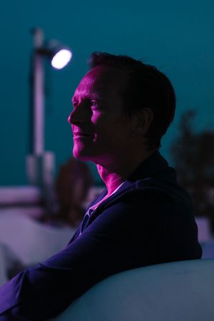 Profile portrait in dramatic purple and blue lighting against a dark background.