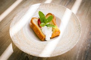 Dessert plate featuring a pastry topped with cream and mint leaf in natural lighting.