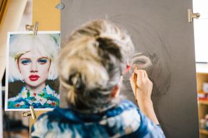Artist working on a detailed portrait drawing with reference photo nearby.