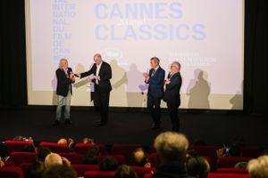 People on stage presenting at the Cannes Classics film event in a theater with red seats.