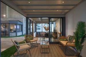Modern outdoor lounge area with rattan furniture and glass walls overlooking a garden.