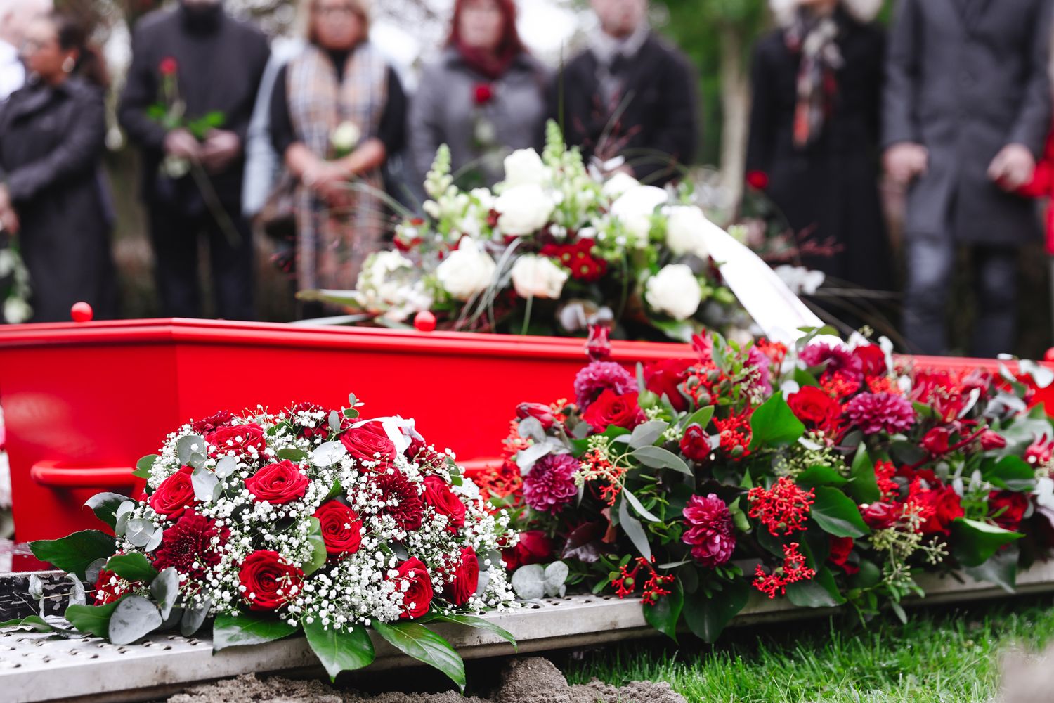 Red casket adorned with beautiful white and red floral arrangements at funeral service.