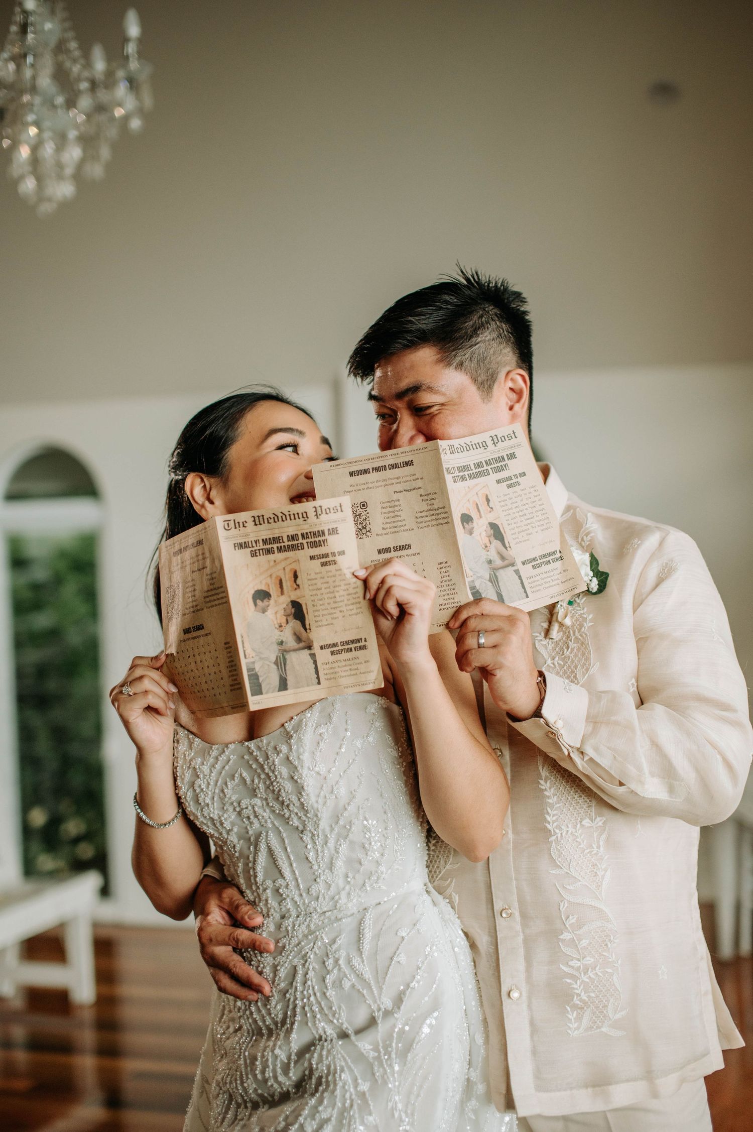 A playful moment as a couple poses with a newspaper covering their faces in a bright venue.