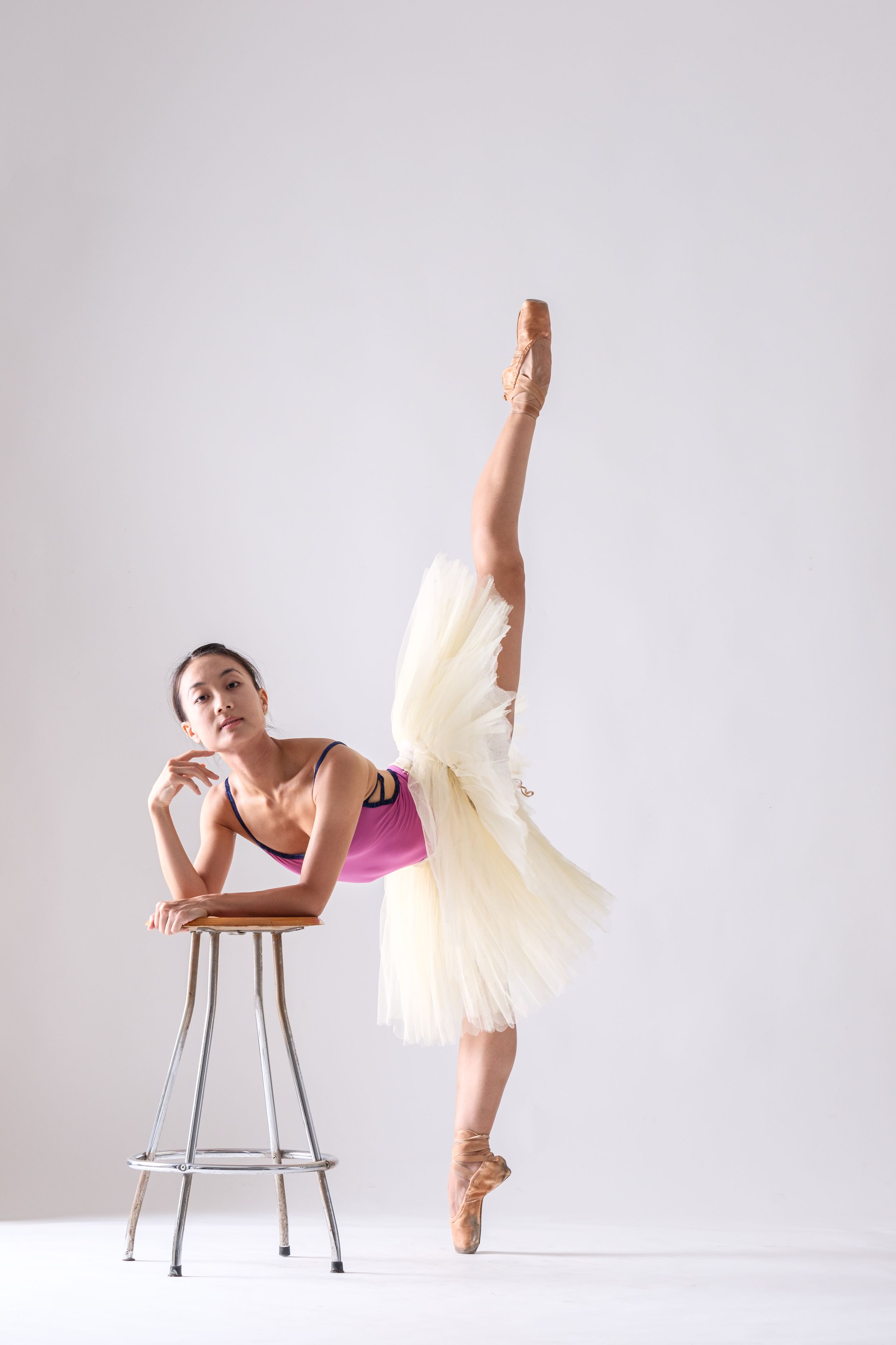 Classical ballet dancer strikes graceful poses with chair in white studio setting.