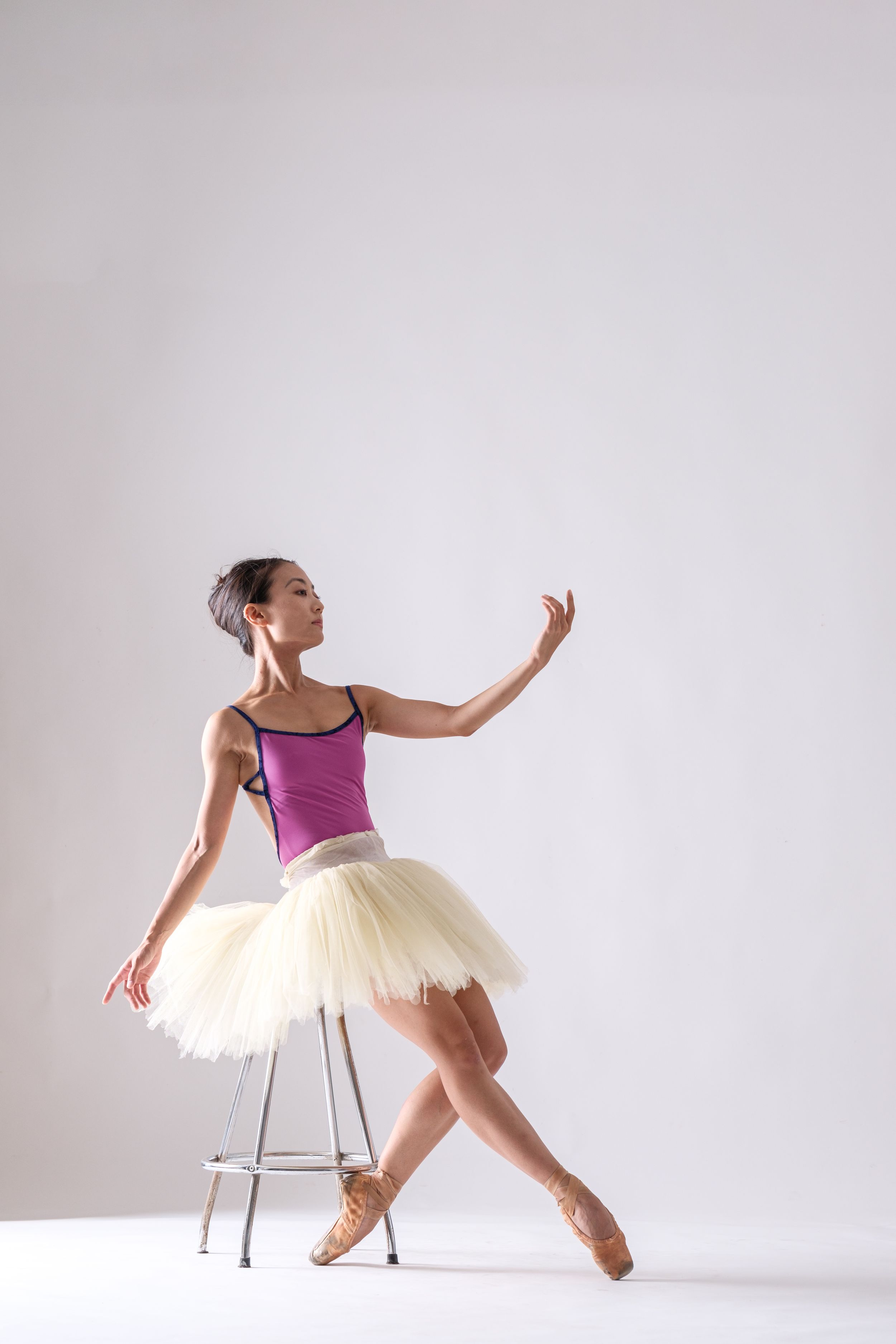Dancer in purple leotard and tutu demonstrates classical ballet positions with chair.