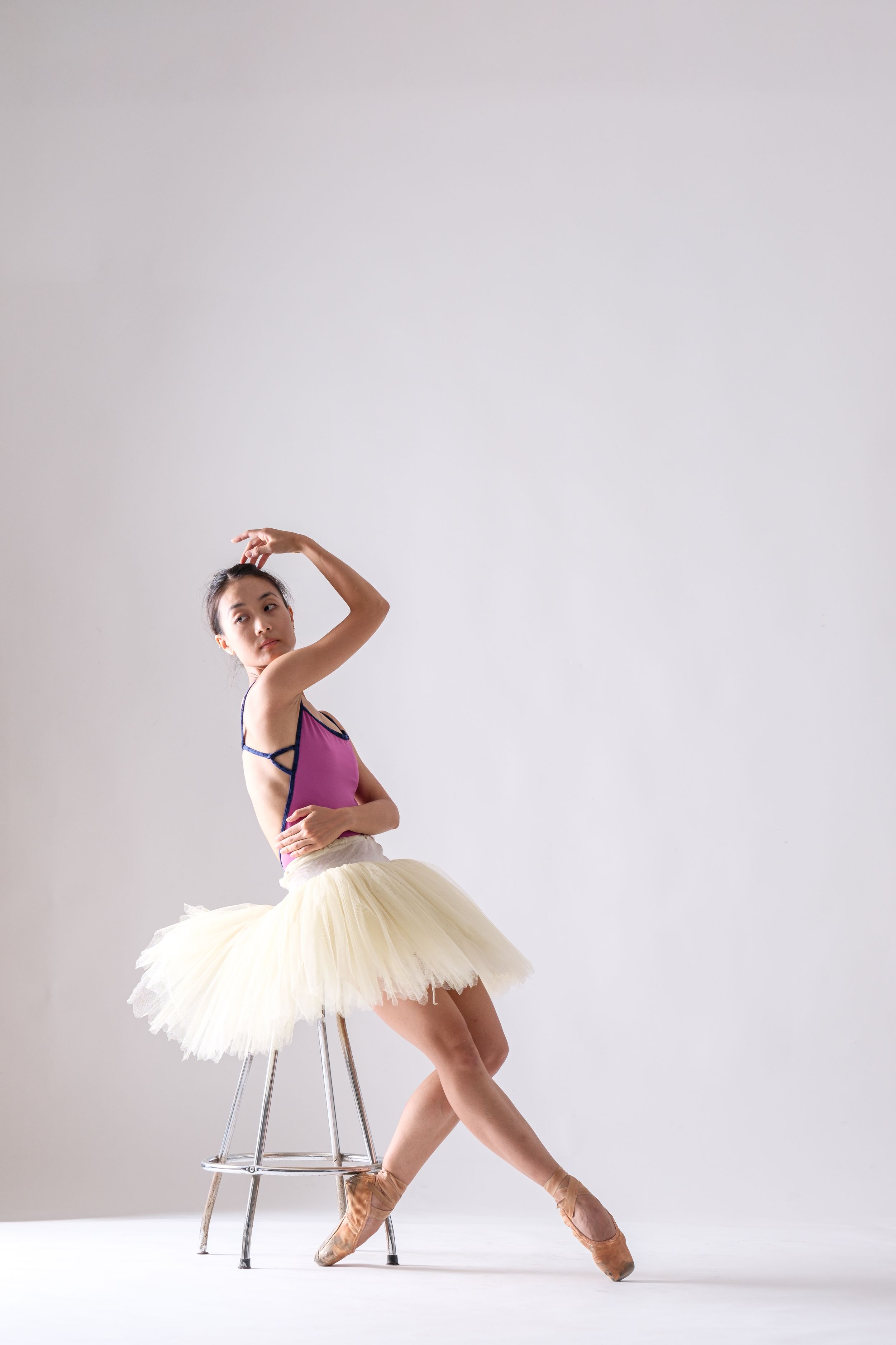 Ballet performer in purple and cream costume creates artistic poses with metal stool.