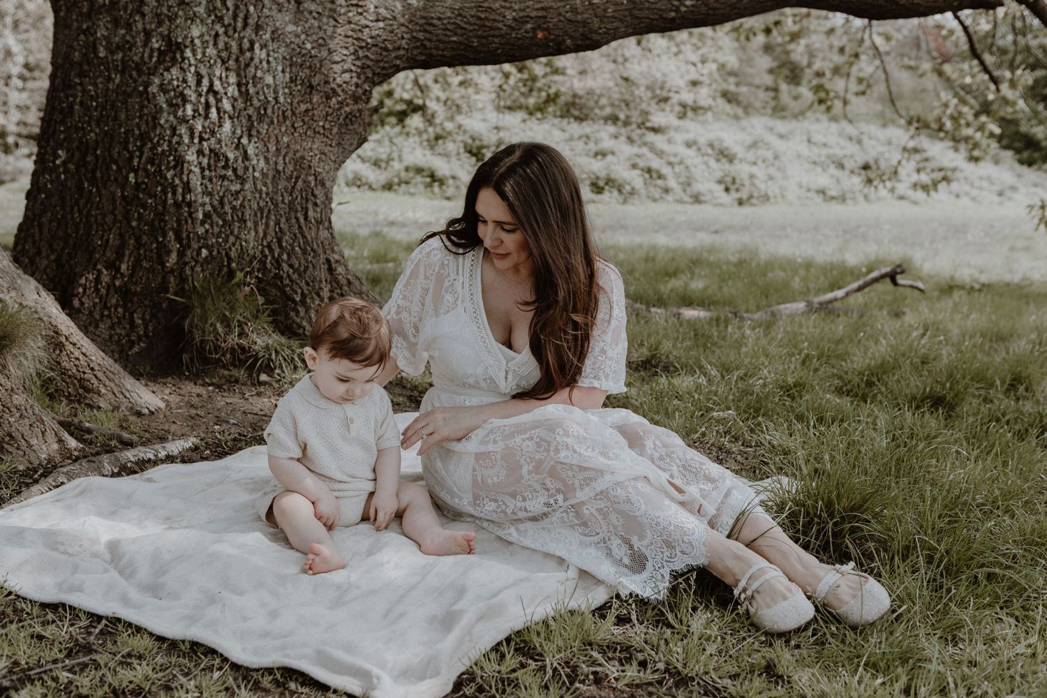 Tender mother-child moment on picnic blanket under large tree in natural setting.