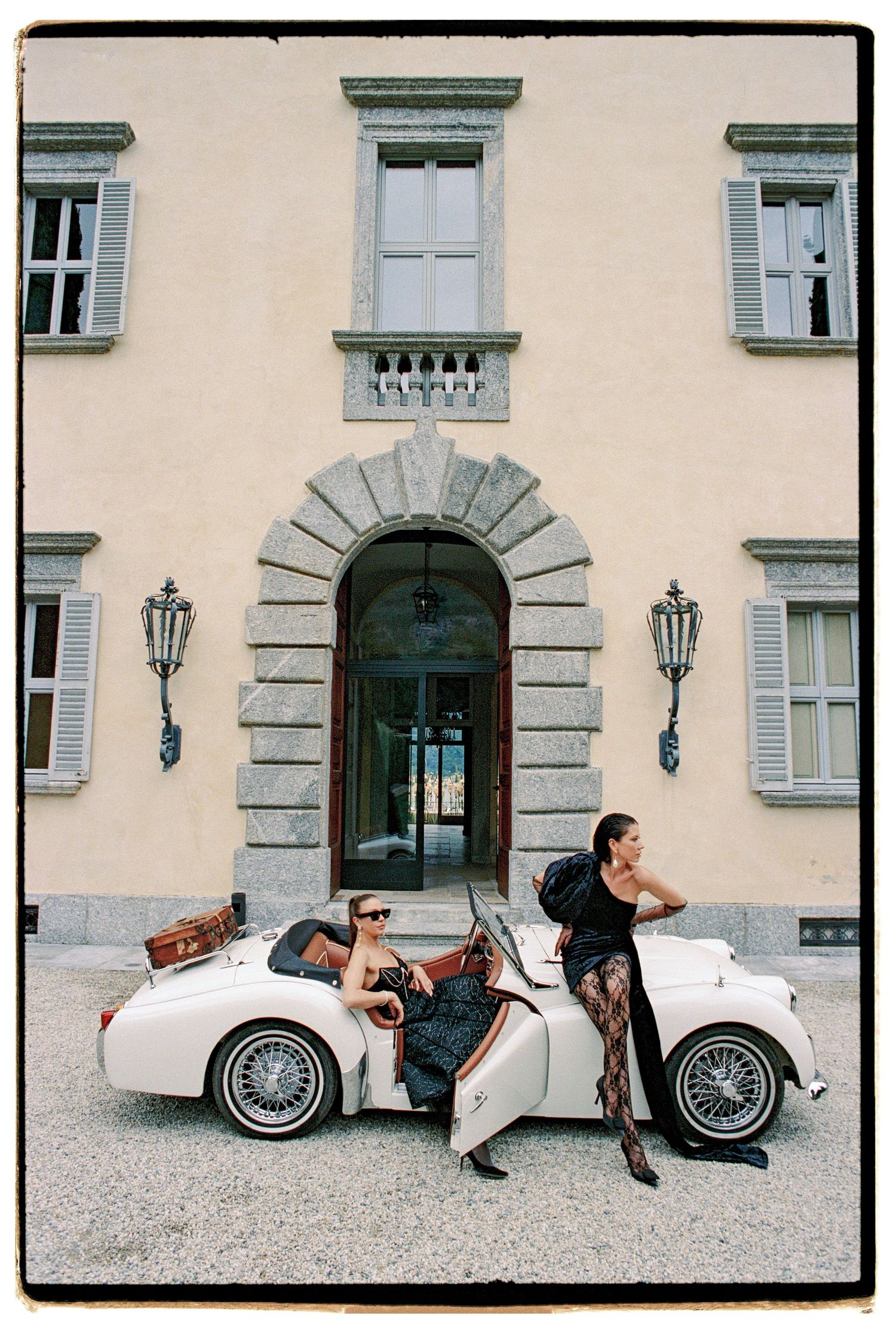 Classic white convertible car parked in front of an elegant Italian villa with traditional architecture and lanterns.
