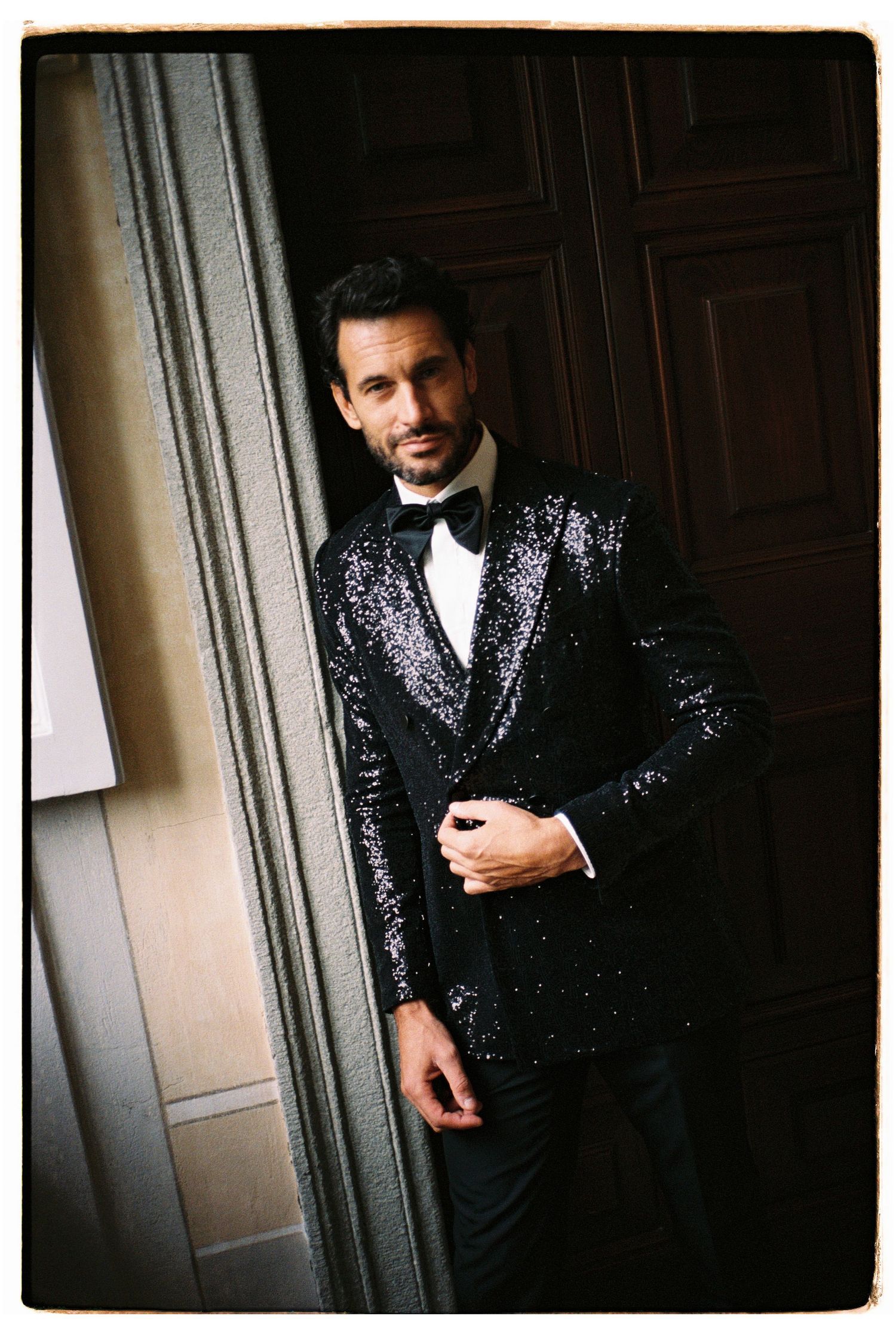 Formal black sequined tuxedo photographed in an elegant interior setting.