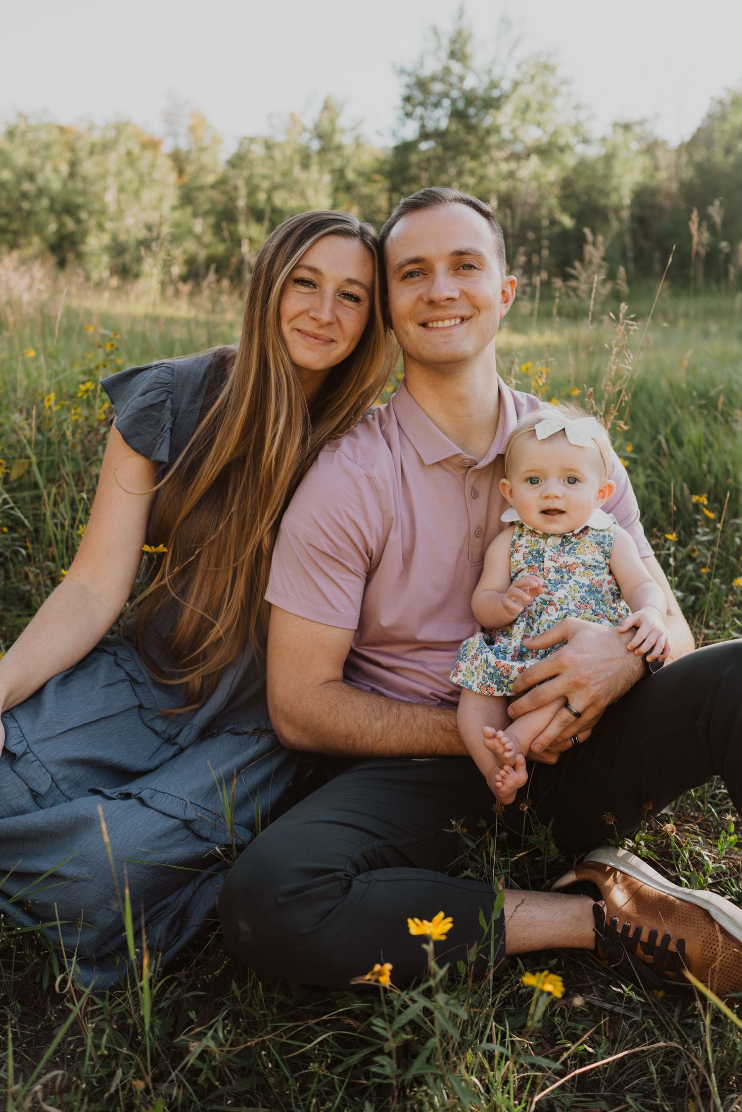 Family relaxing together on blanket in field with yellow wildflowers during golden hour.