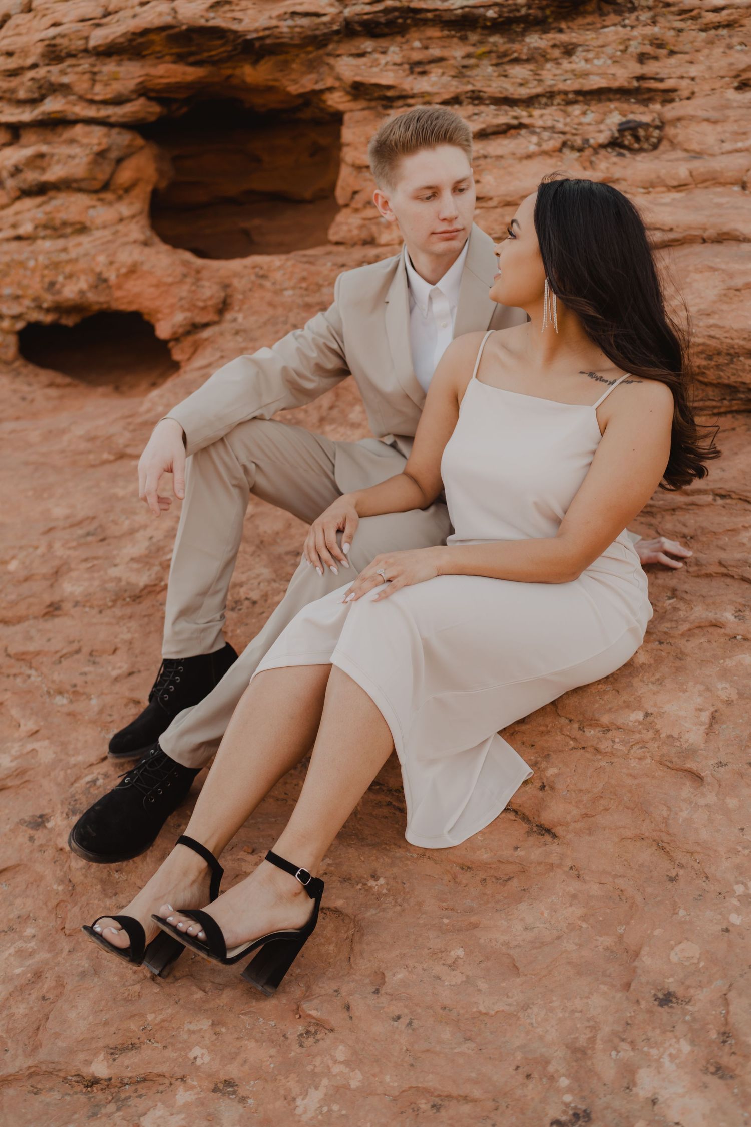 Couple in light summer attire sitting on red rock formation.