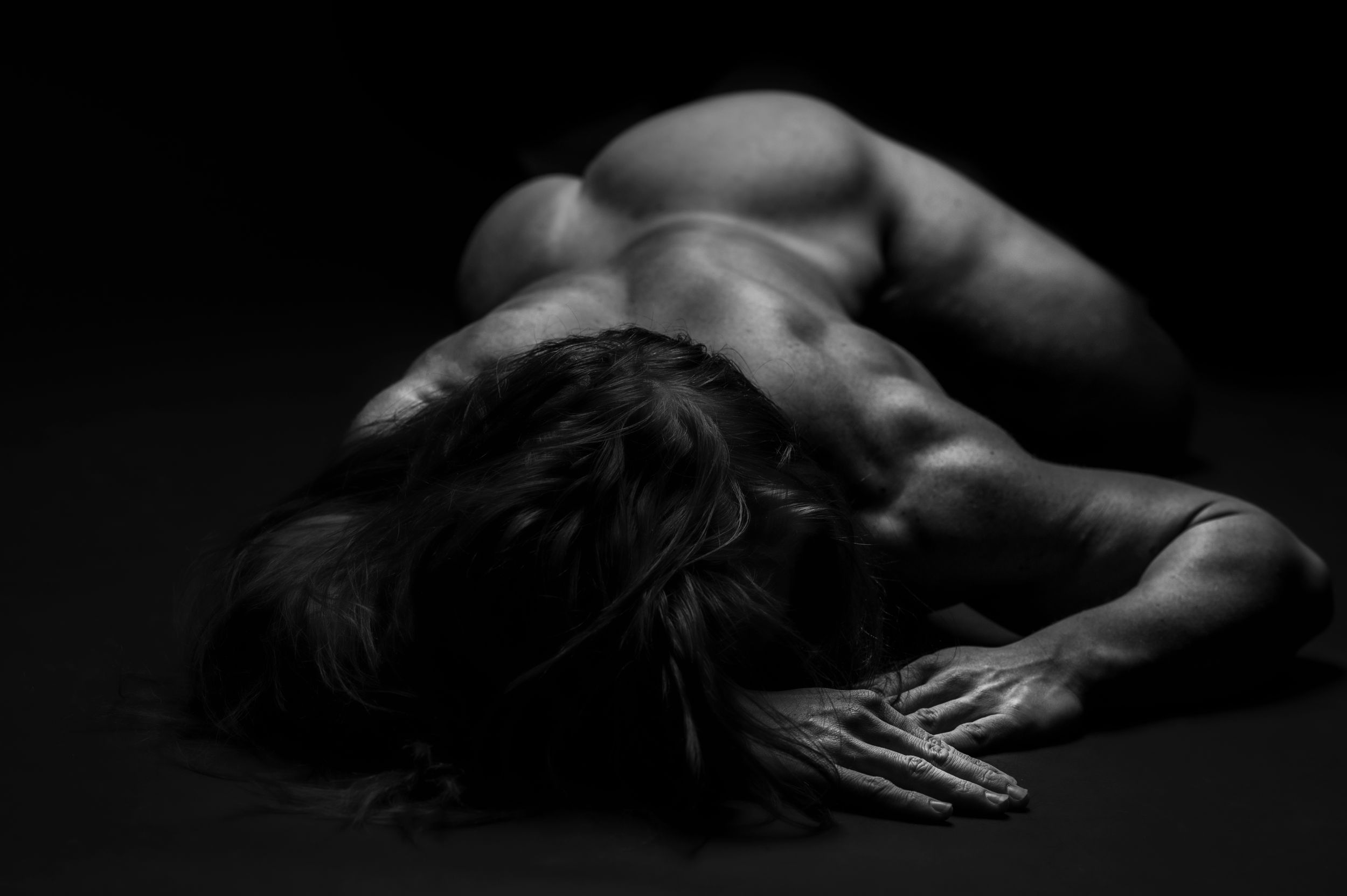 Artistic nude bodyscape photography showing dramatic shadows and contours in monochrome.