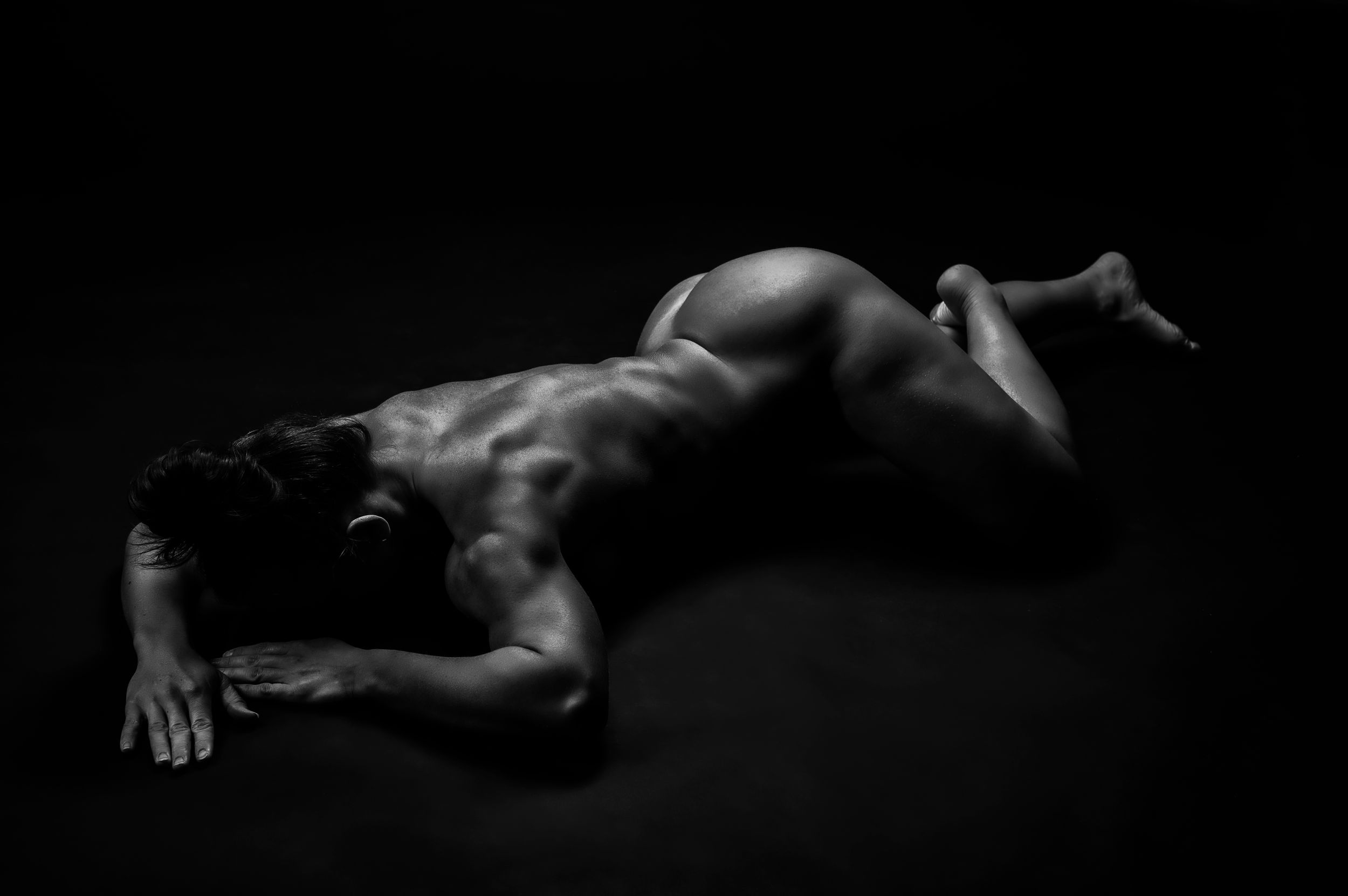 Black and white artistic nude study with dramatic lighting and shadows.