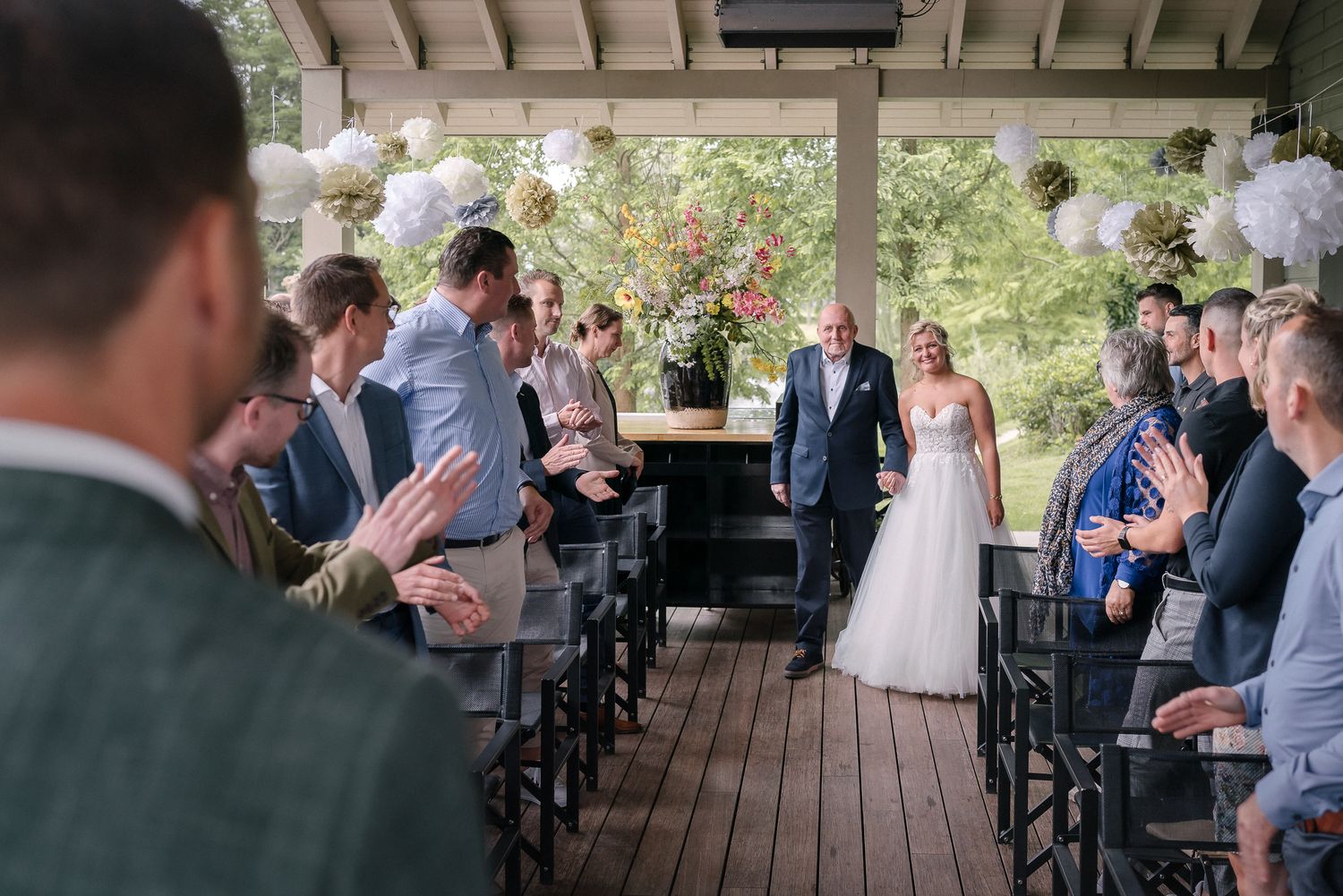 Wedding ceremony attendees gathered on a wooden deck surrounded by trees and natural scenery.
