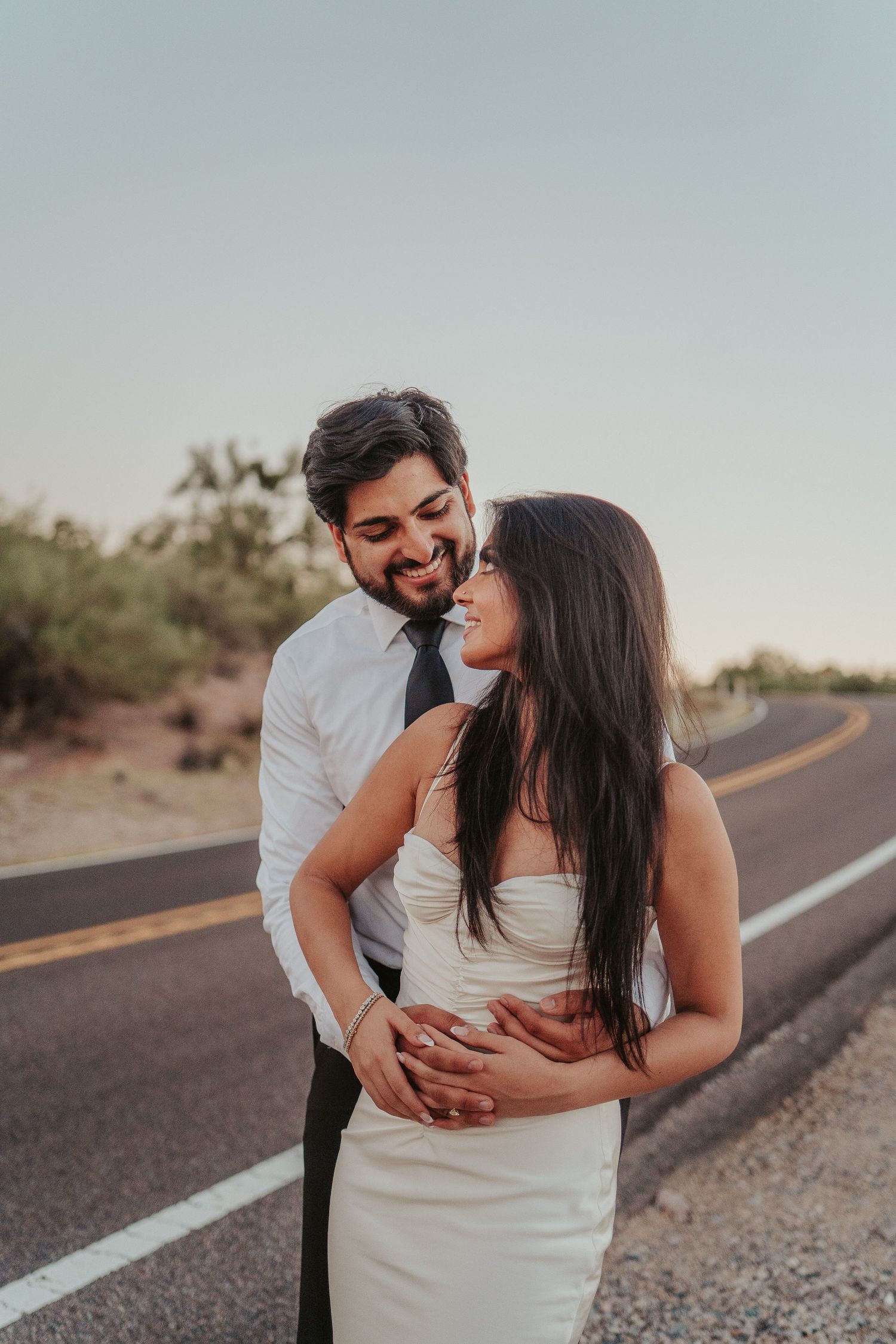 A couple embraces and laughs together on a desert road at sunset.