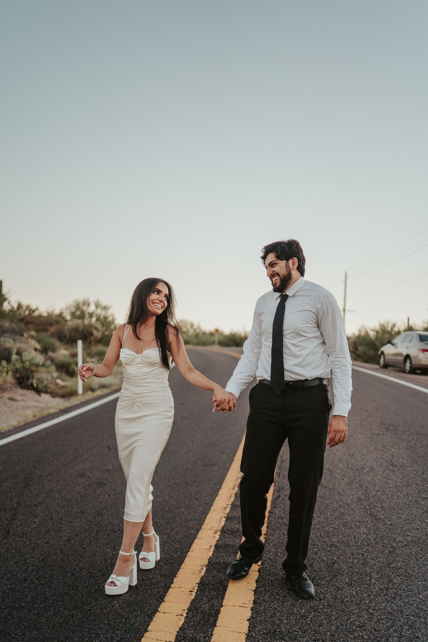 Couple holding hands while walking on desert road in formal attire.