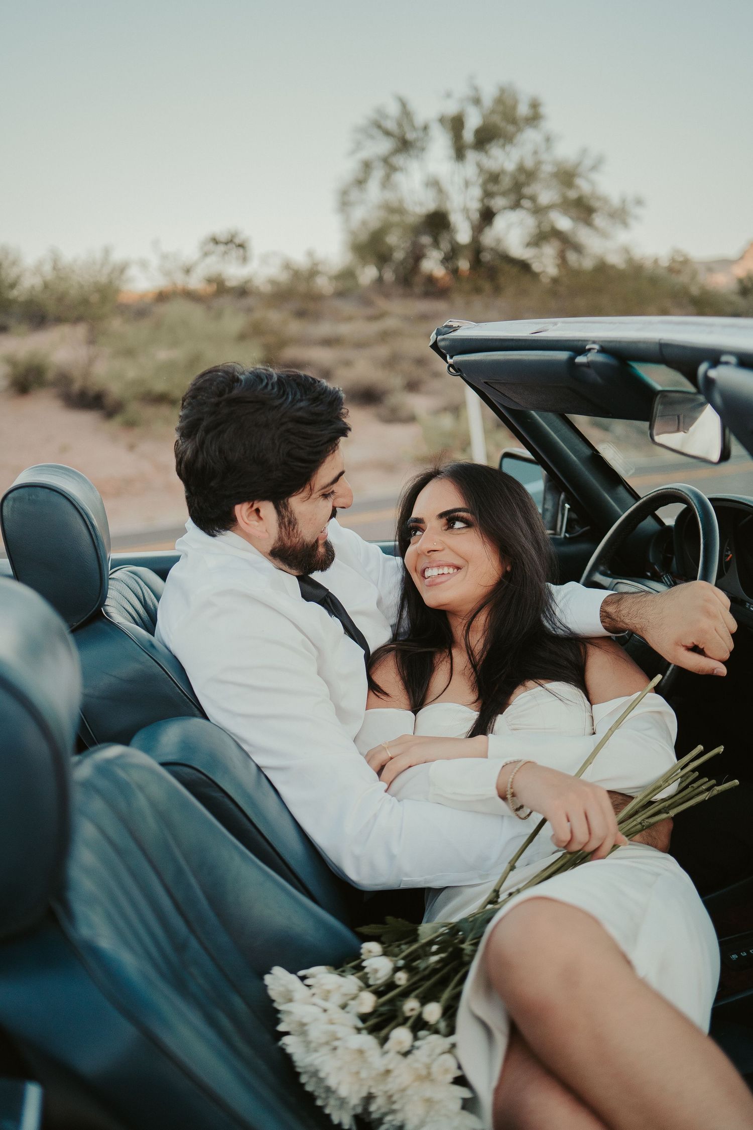 Romantic desert wedding photoshoot in vintage convertible with white flowers.