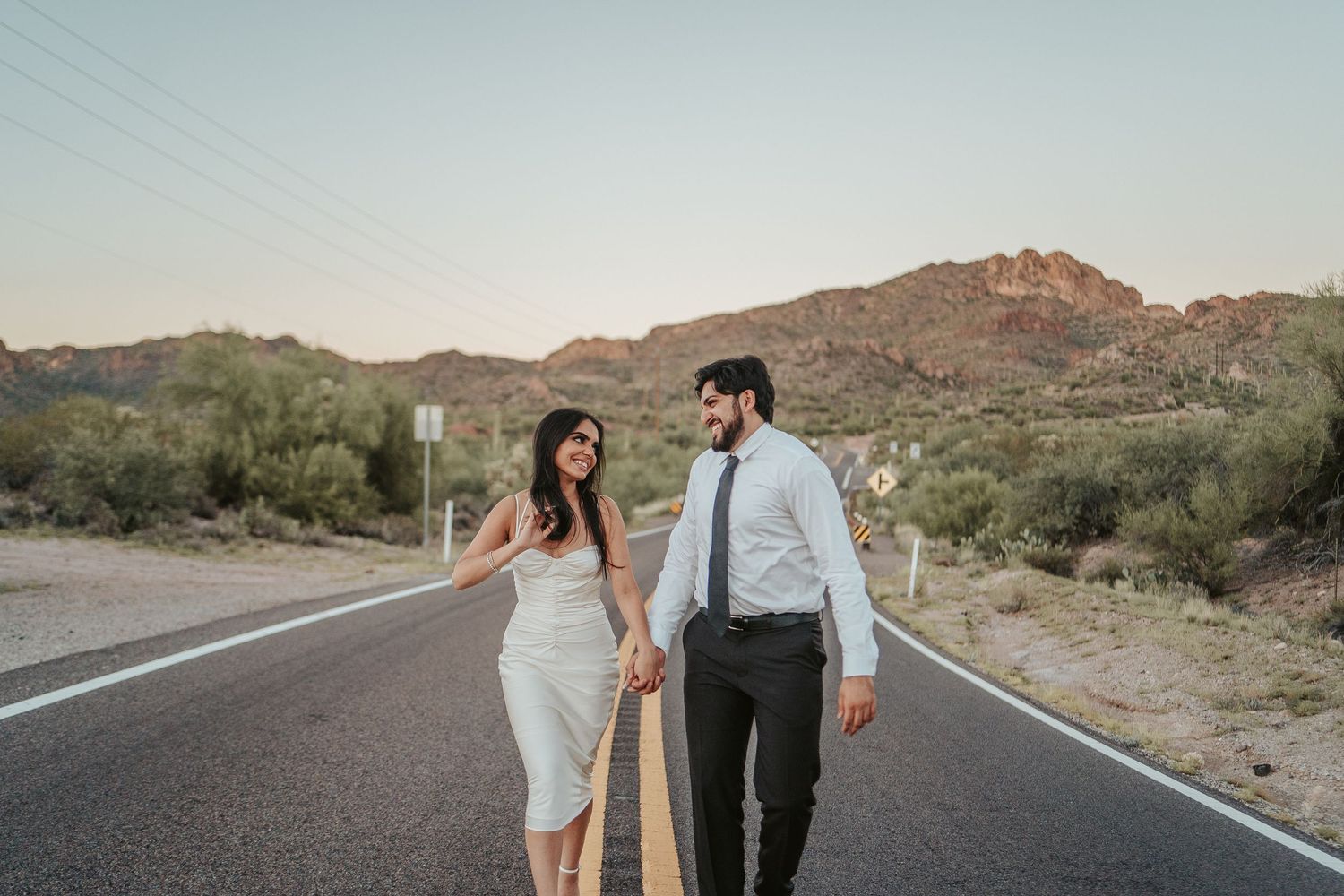 Couple in wedding attire holding hands while walking on desert road.