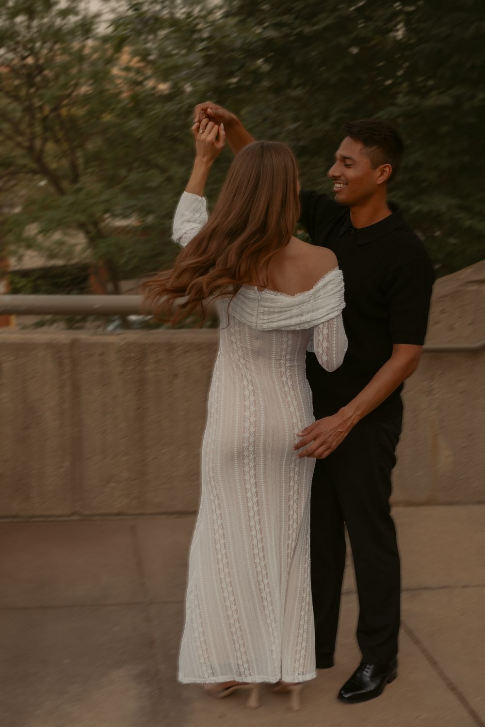A couple in formal wear dances together on a pathway during a romantic outdoor photoshoot.