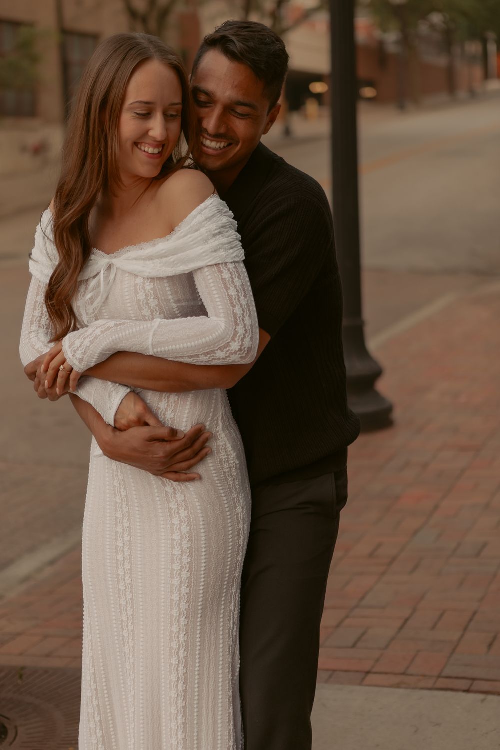 A romantic moment captured between a couple embracing and laughing together on a brick pathway.