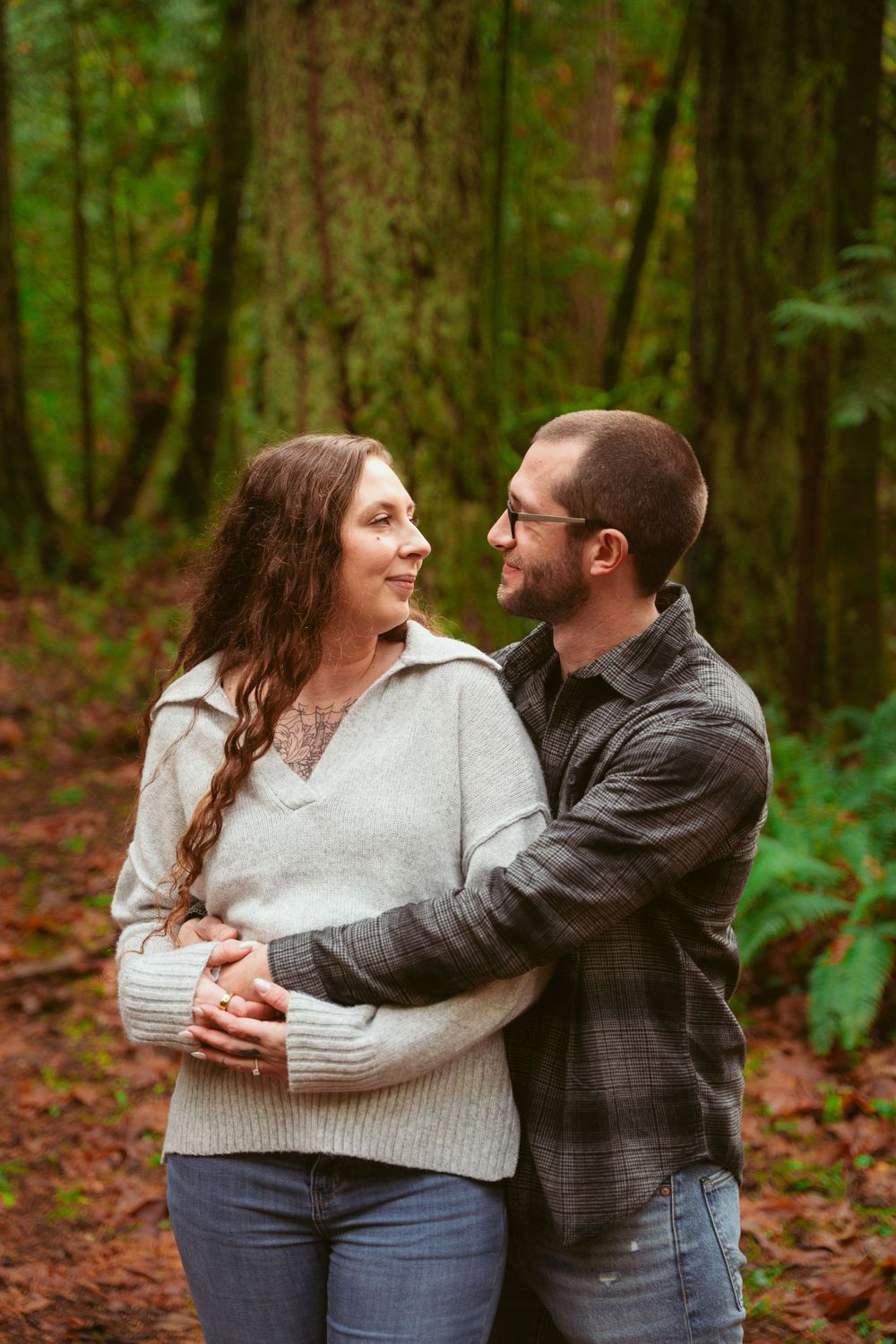 A couple shares a loving embrace while standing together in a lush forest setting on an autumn day.