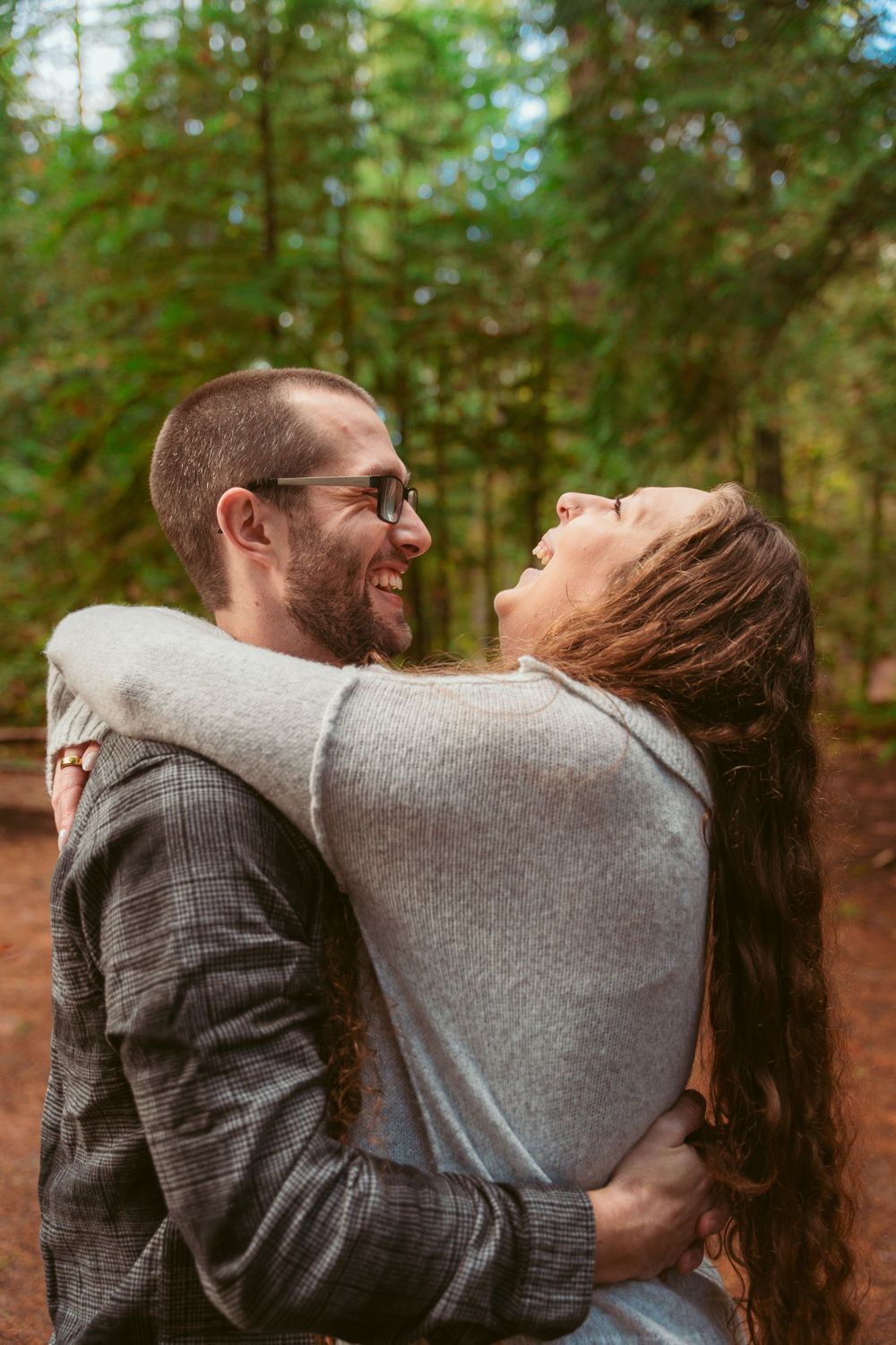 Happy couple embracing and laughing together in a wooded forest setting.