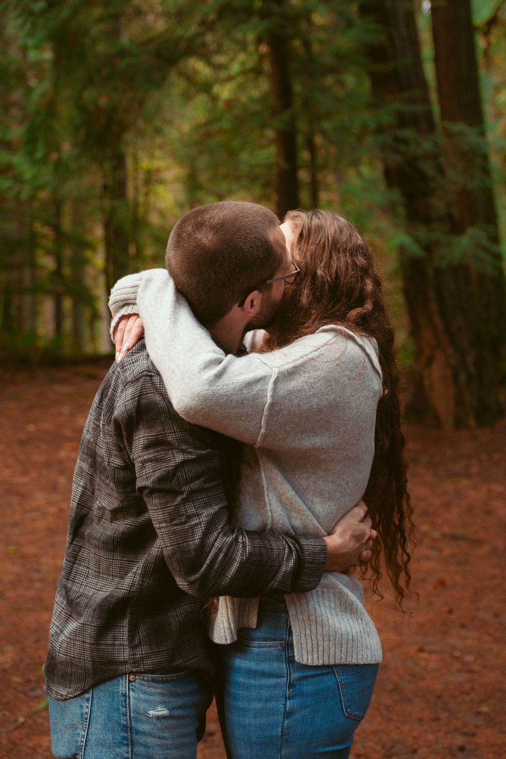 A couple embracing in a romantic moment on a trail through an autumn forest with fallen red leaves.