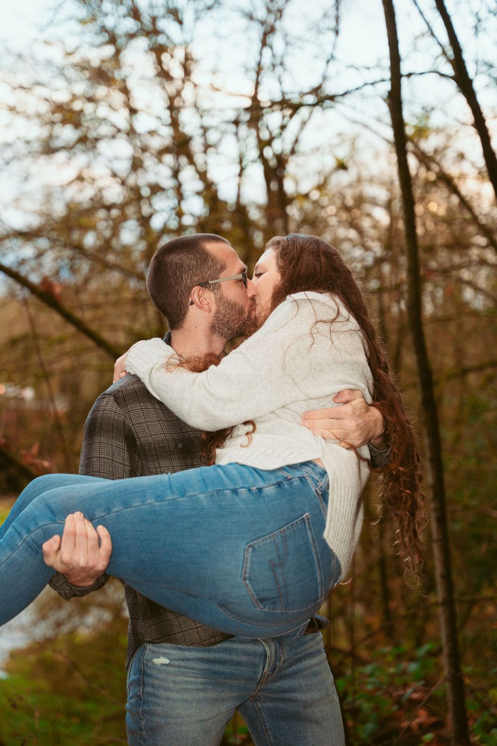 A romantic outdoor scene of two people sharing a kiss while one is held in a dip pose against a forest backdrop.