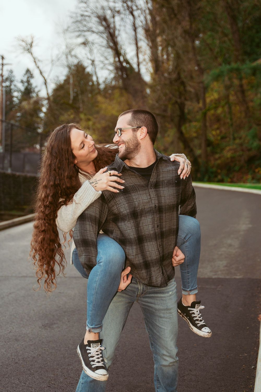 A couple dances playfully on a paved road surrounded by autumn trees in the background.