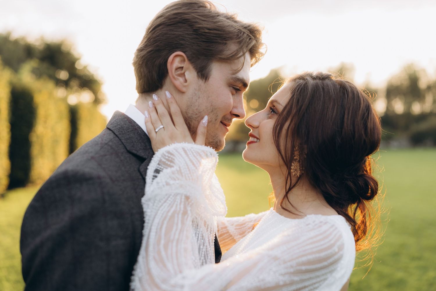 A couple in wedding attire share an intimate moment in a sunlit meadow at golden hour.