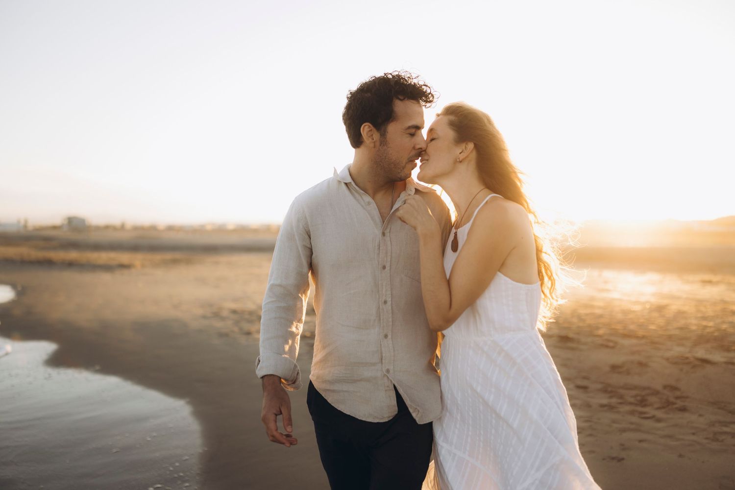 A couple shares an intimate moment at the beach during golden hour.