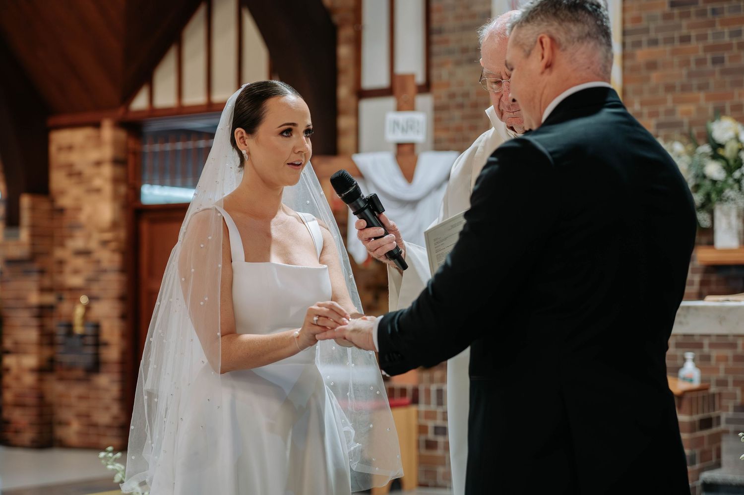Modern church wedding ceremony with guests seated in wooden pews beneath vaulted ceiling with warm lighting.